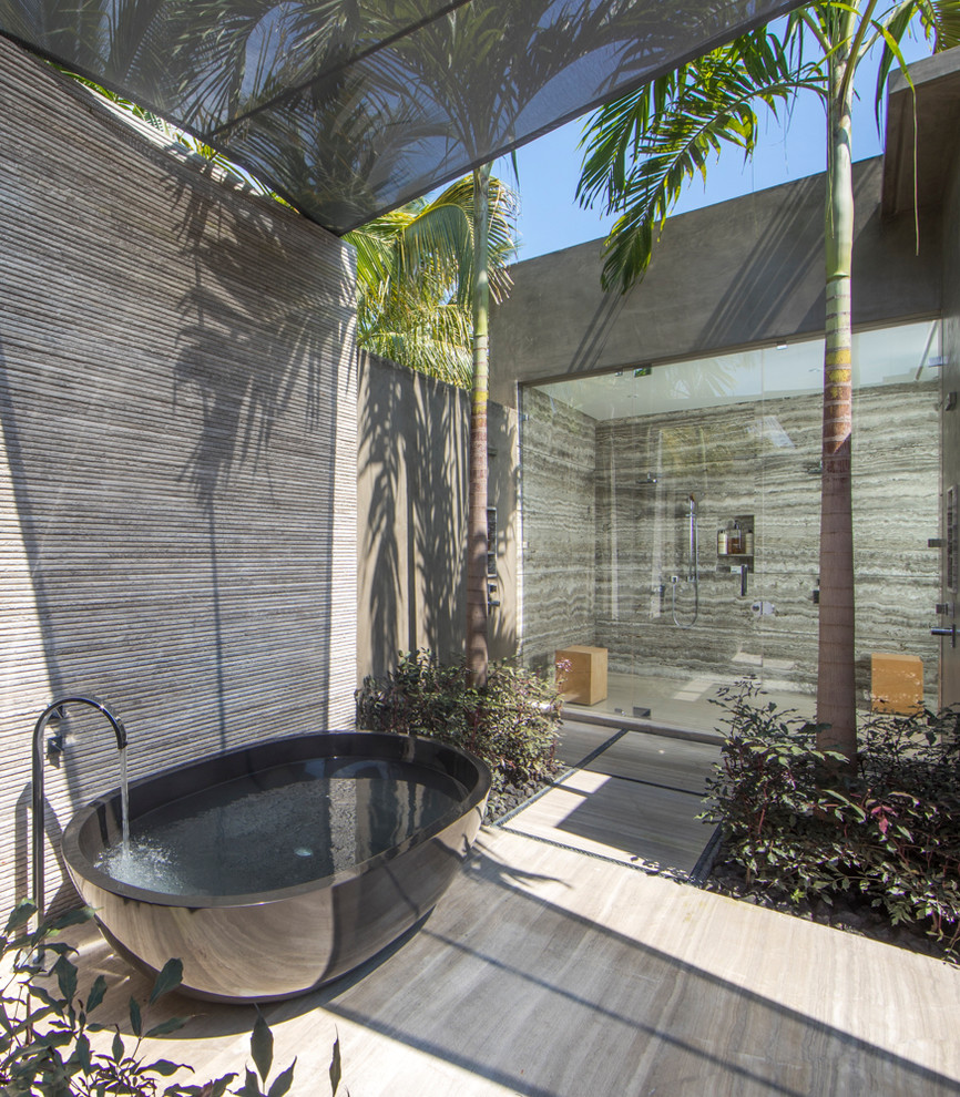 Photo of an expansive tropical master wet room bathroom in Mexico City with a freestanding tub, gray tile, grey walls, beige floor and a hinged shower door.