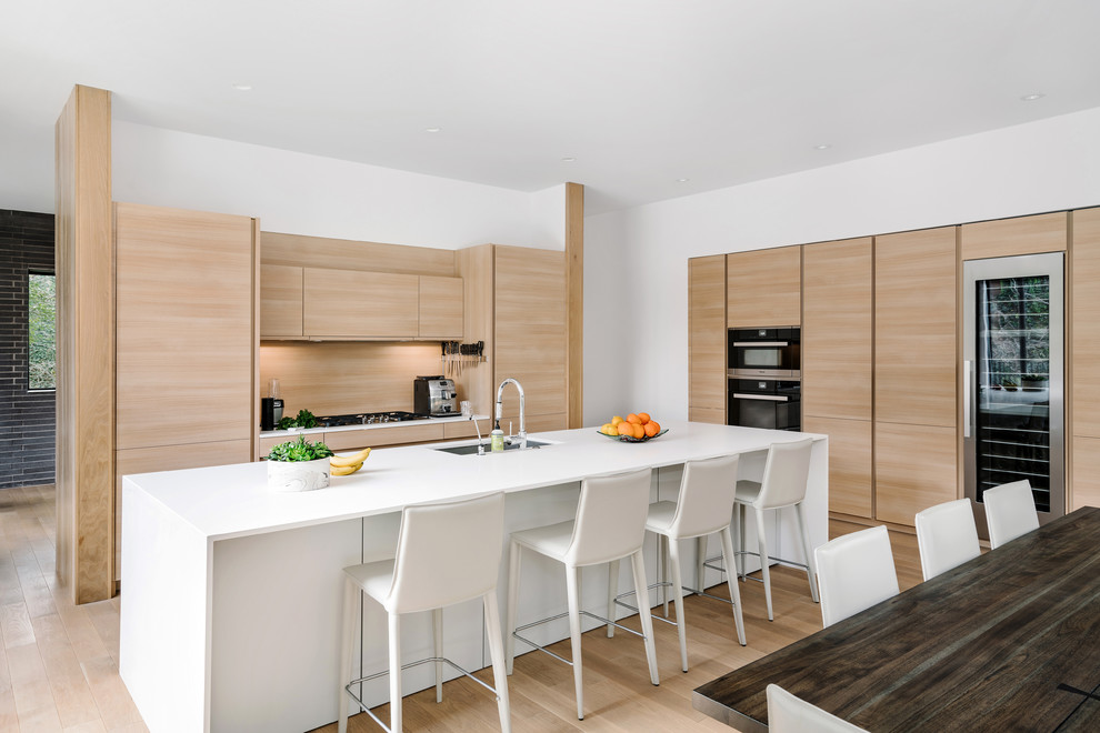 This is an example of a contemporary l-shaped eat-in kitchen in Austin with an undermount sink, flat-panel cabinets, light wood cabinets, timber splashback, black appliances, light hardwood floors and with island.