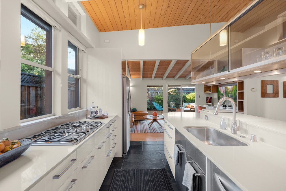 Inspiration for a midcentury kitchen in Other with flat-panel cabinets, white cabinets, quartz benchtops, stainless steel appliances, slate floors, a peninsula, black floor, white benchtop and exposed beam.