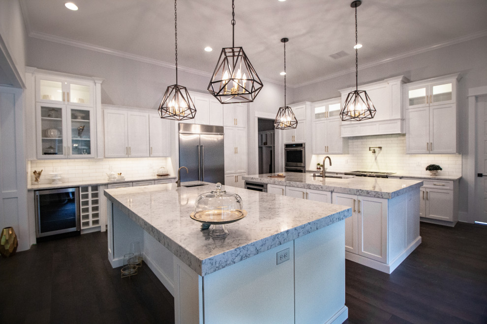 Photo of a large transitional u-shaped eat-in kitchen in Jacksonville with an undermount sink, recessed-panel cabinets, white cabinets, quartz benchtops, white splashback, subway tile splashback, stainless steel appliances, dark hardwood floors, multiple islands, brown floor and grey benchtop.