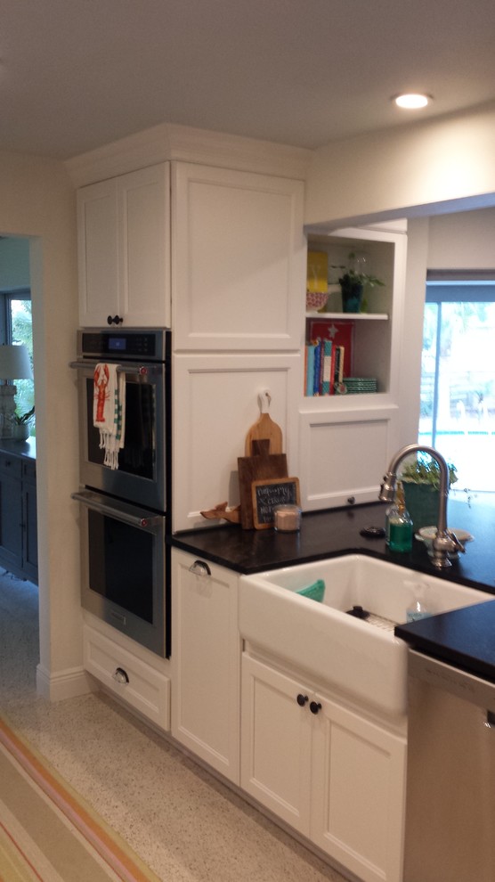 Example of a transitional galley kitchen design in Tampa with a farmhouse sink, recessed-panel cabinets, white cabinets, granite countertops, beige backsplash, glass tile backsplash and paneled appliances