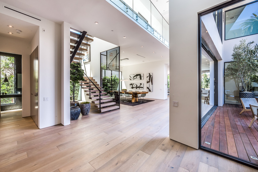 This is an example of a large modern foyer in Los Angeles with white walls, light hardwood floors, a single front door and a glass front door.