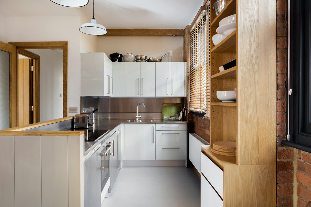 Small contemporary kitchen in London with an integrated sink, flat-panel cabinets, white cabinets, stainless steel benchtops, metallic splashback, a peninsula, grey floor and grey benchtop.