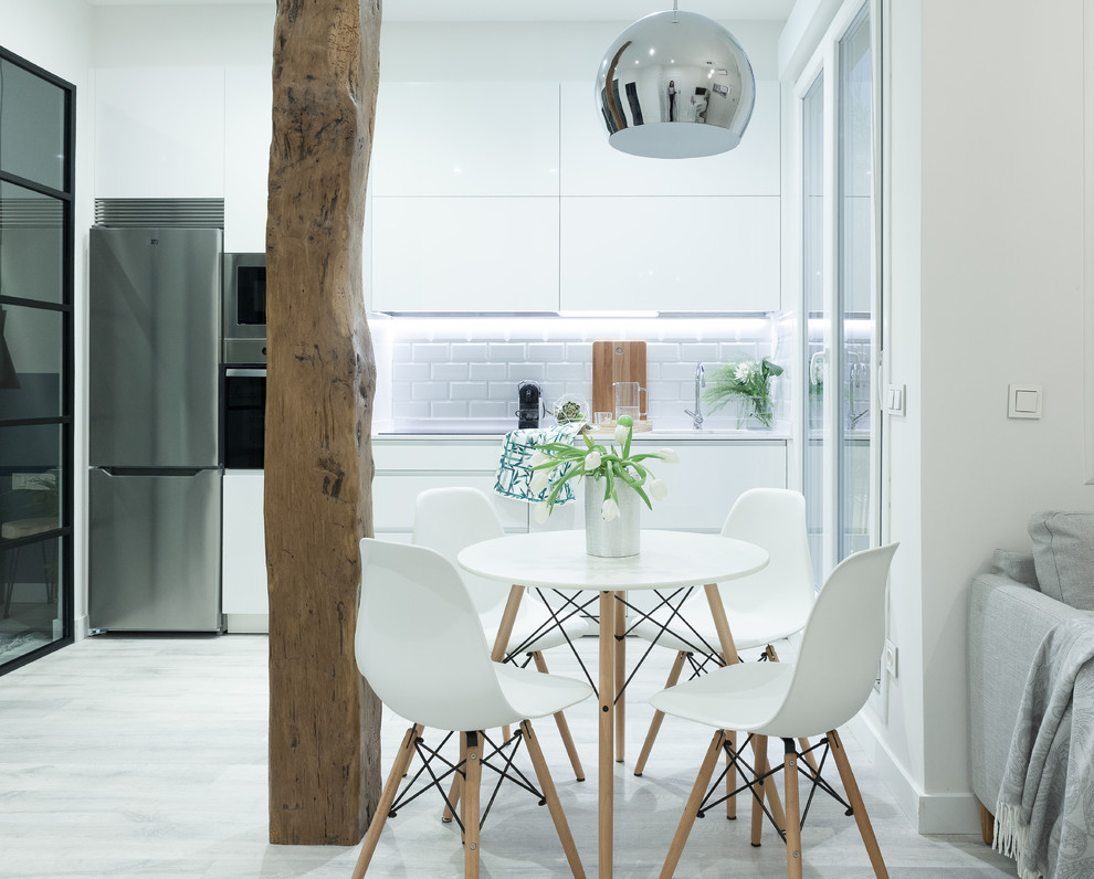 Design ideas for a mid-sized scandinavian single-wall open plan kitchen in Madrid with an undermount sink, flat-panel cabinets, white cabinets, white splashback, ceramic splashback, stainless steel appliances, laminate floors and grey floor.