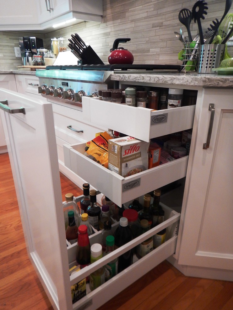 Example of a large transitional l-shaped light wood floor eat-in kitchen design with an undermount sink, recessed-panel cabinets, white cabinets, quartz countertops, gray backsplash, stone tile backsplash, stainless steel appliances and an island