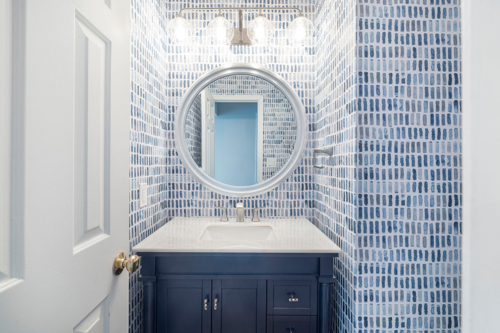 Inspiration for a small beach style powder room in DC Metro with furniture-like cabinets, blue cabinets, a one-piece toilet, blue tile, multi-coloured walls, medium hardwood floors, an undermount sink, engineered quartz benchtops, brown floor, white benchtops, a freestanding vanity and wallpaper.