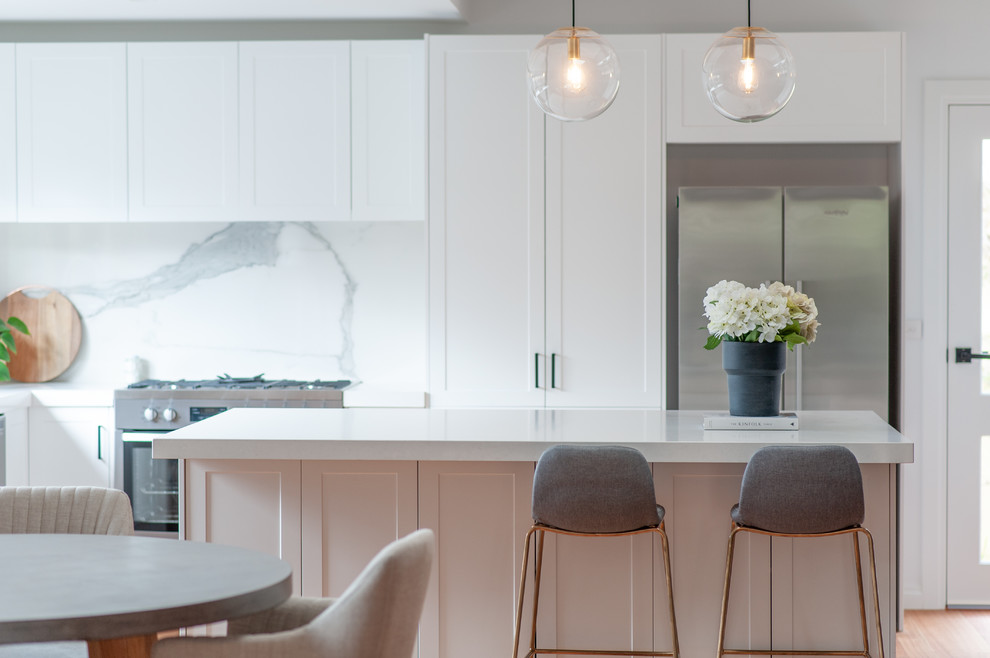 Design ideas for a large transitional u-shaped kitchen pantry in Melbourne with an undermount sink, recessed-panel cabinets, white cabinets, white splashback, stone slab splashback, stainless steel appliances, medium hardwood floors, with island and white benchtop.