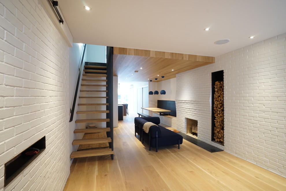 Mid-sized modern open concept family room in New York with white walls, light hardwood floors, a standard fireplace, a brick fireplace surround, no tv and brown floor.