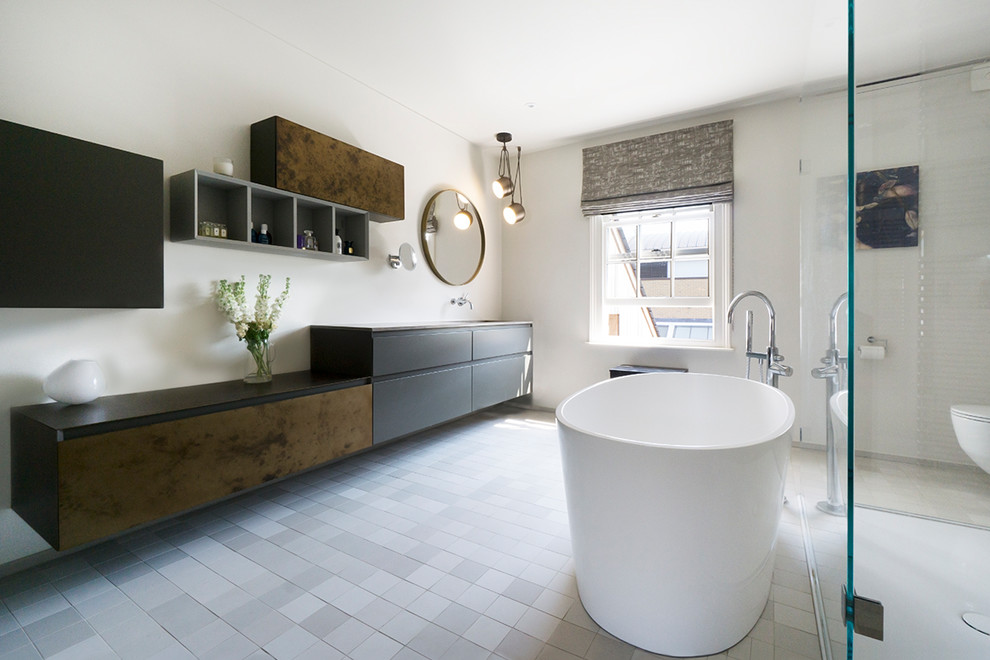 This is an example of a mid-sized contemporary master bathroom in Cambridgeshire with flat-panel cabinets, black cabinets, a freestanding tub, white walls, grey floor, a curbless shower and black benchtops.