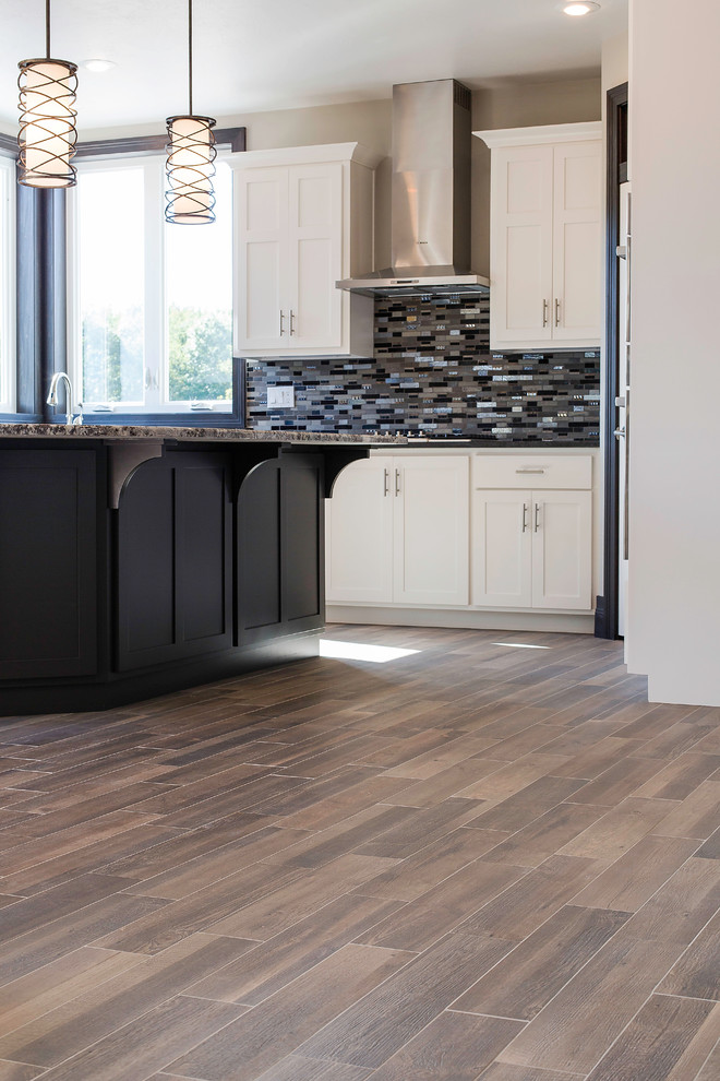 Example of a large transitional light wood floor and brown floor kitchen design with granite countertops, multicolored backsplash, glass tile backsplash, stainless steel appliances, an island and white cabinets