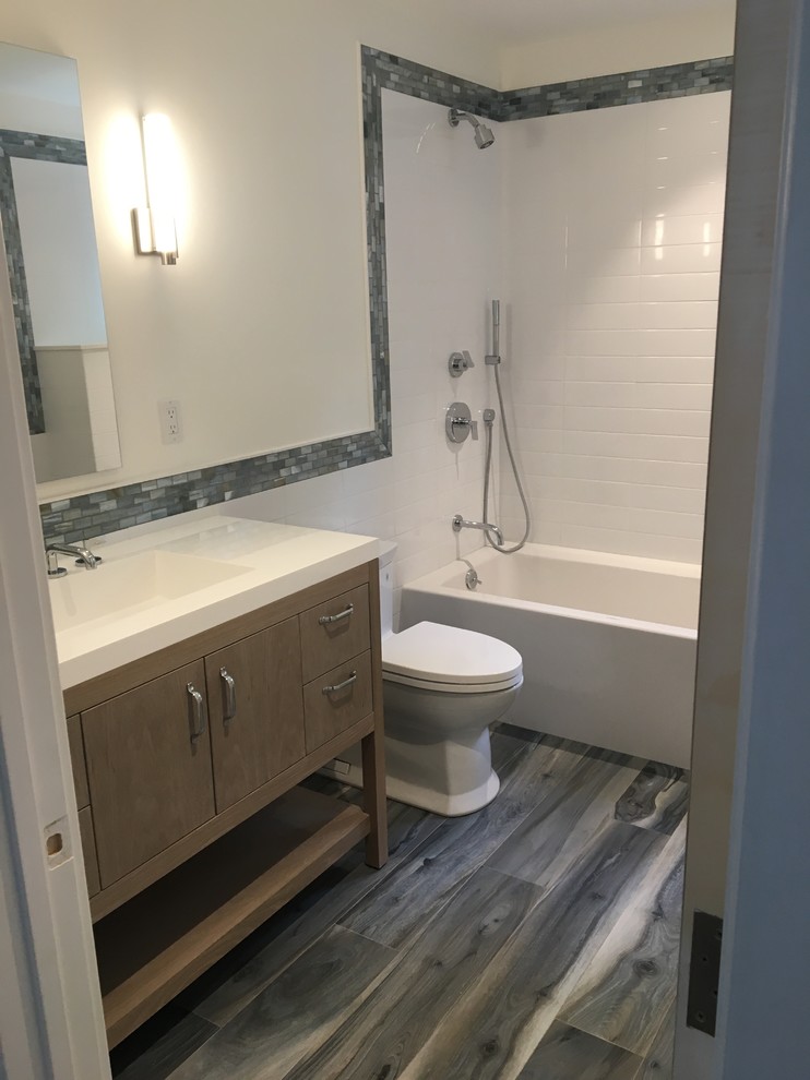 Design ideas for a mid-sized transitional 3/4 bathroom in New York with flat-panel cabinets, light wood cabinets, an alcove tub, a shower/bathtub combo, a one-piece toilet, white tile, subway tile, white walls, dark hardwood floors, an integrated sink, solid surface benchtops and black floor.