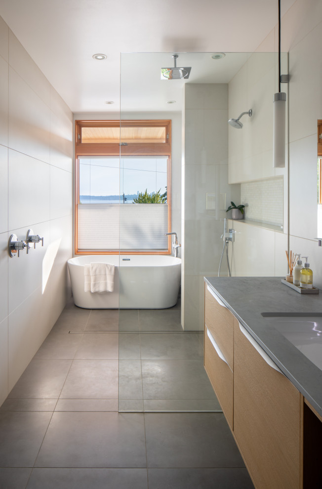 Photo of a mid-sized modern master bathroom in Seattle with flat-panel cabinets, light wood cabinets, a freestanding tub, a shower/bathtub combo, white tile, ceramic tile, porcelain floors, an undermount sink, solid surface benchtops, grey floor, an open shower, grey benchtops, a double vanity and a floating vanity.