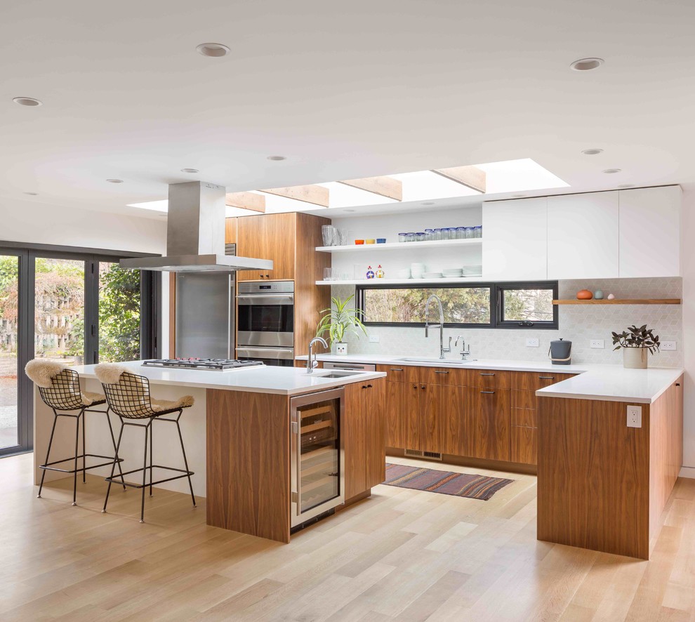 Midcentury l-shaped kitchen in Portland with an undermount sink, flat-panel cabinets, medium wood cabinets, white splashback, stainless steel appliances, light hardwood floors, with island, beige floor and white benchtop.