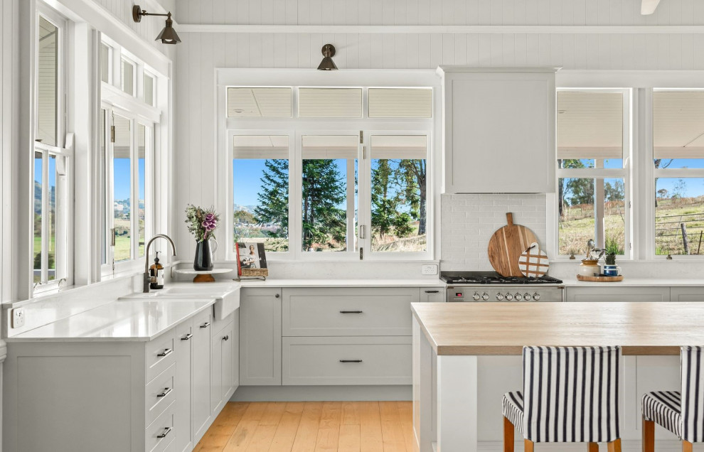 Design ideas for a mid-sized country l-shaped kitchen pantry in Sunshine Coast with a farmhouse sink, shaker cabinets, green cabinets, quartz benchtops, white splashback, engineered quartz splashback, stainless steel appliances, medium hardwood floors, with island, yellow floor, white benchtop and timber.