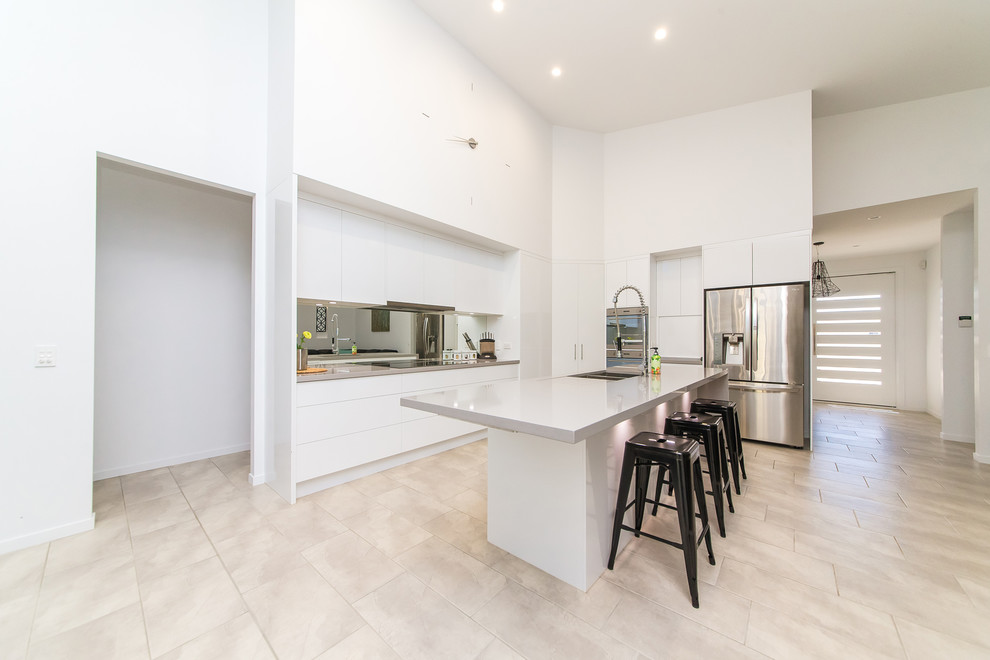 Mid-sized modern l-shaped eat-in kitchen in Brisbane with flat-panel cabinets, white cabinets, metallic splashback, mirror splashback, with island, an undermount sink, quartz benchtops and travertine floors.