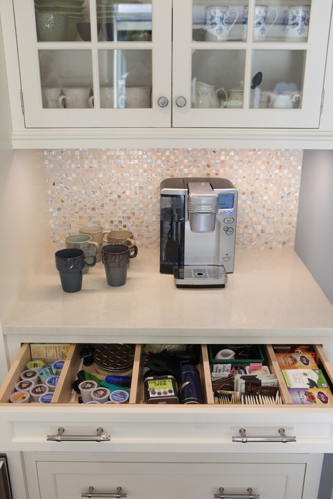 Large transitional l-shaped eat-in kitchen in New York with a double-bowl sink, recessed-panel cabinets, white cabinets, solid surface benchtops, white splashback, mosaic tile splashback, stainless steel appliances, porcelain floors and with island.