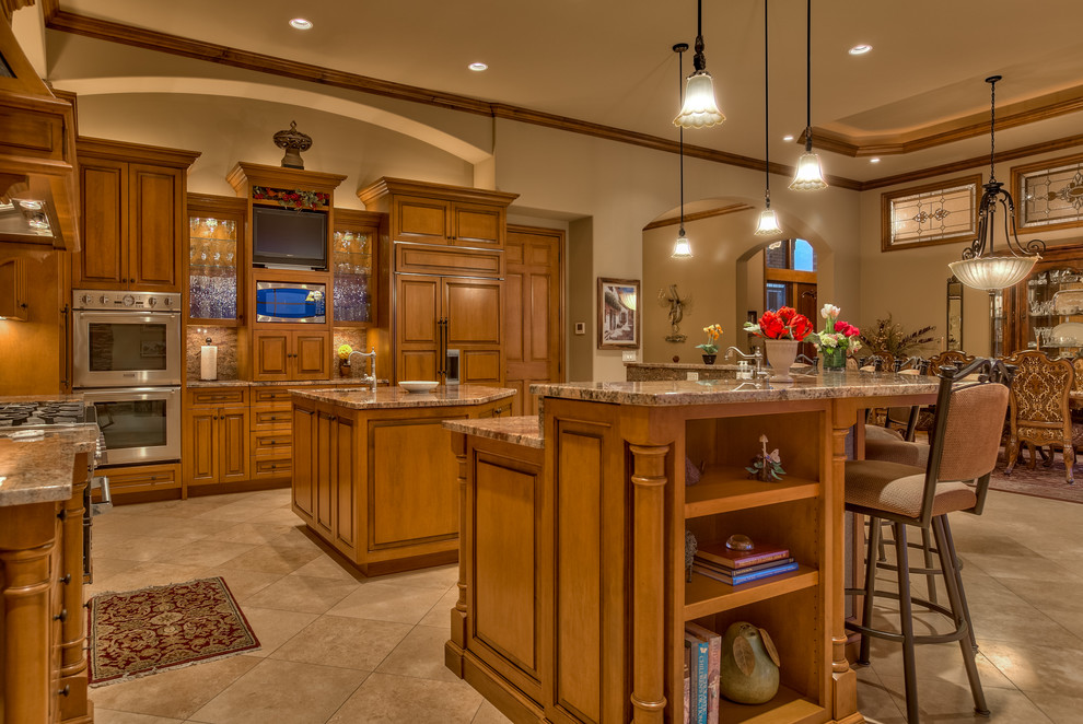 This is an example of a large traditional l-shaped eat-in kitchen in Omaha with an undermount sink, recessed-panel cabinets, medium wood cabinets, granite benchtops, brown splashback, stone slab splashback, stainless steel appliances, porcelain floors, multiple islands and beige floor.