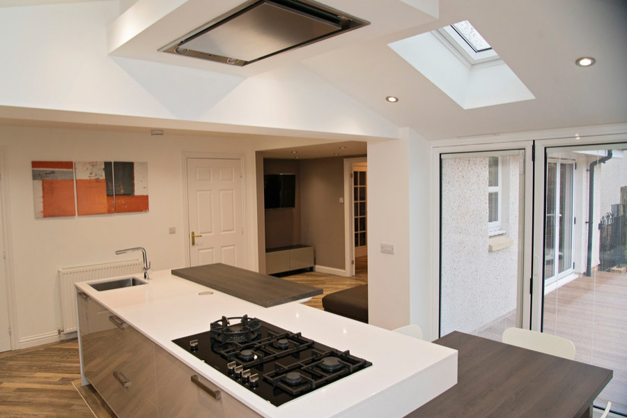Inspiration for a large contemporary single-wall open plan kitchen in Other with a submerged sink, flat-panel cabinets, white cabinets, quartz worktops, black splashback, glass sheet splashback, black appliances, light hardwood flooring, an island, multi-coloured floors, white worktops and exposed beams.