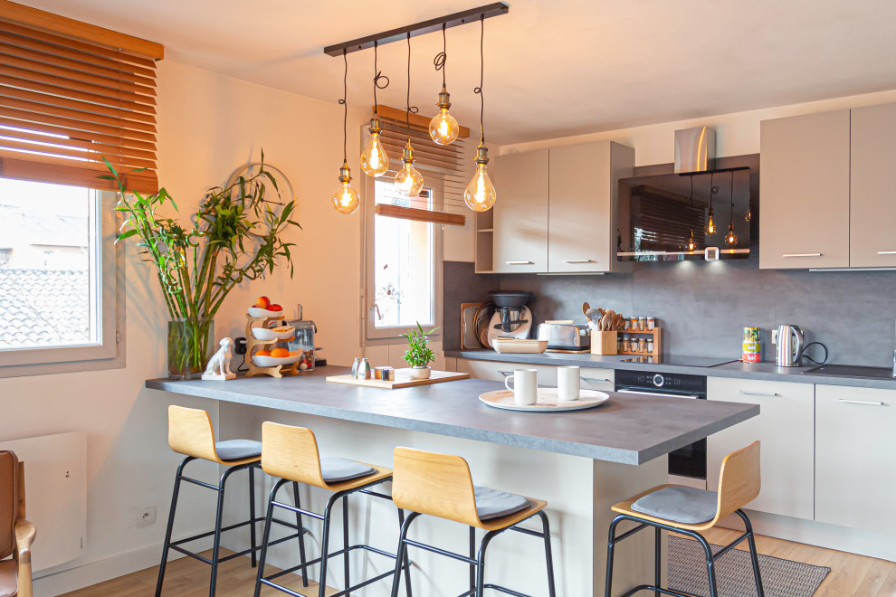 Стильный дизайн: параллельная кухня-гостиная среднего размера в современном стиле с врезной мойкой, серыми фасадами, столешницей из бетона, серым фартуком, черной техникой, светлым паркетным полом, островом и серой столешницей - последний тренд