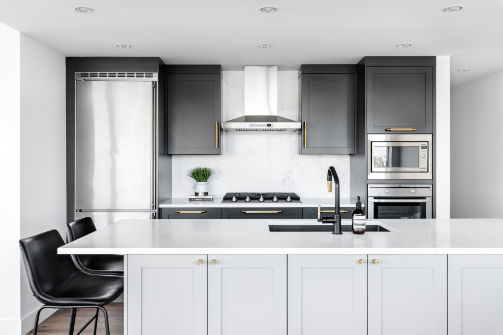Transitional kitchen in Vancouver with an undermount sink, shaker cabinets, black cabinets, white splashback, stone slab splashback, stainless steel appliances, medium hardwood floors, with island and white benchtop.