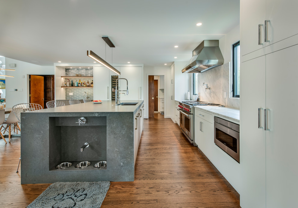 Foto på ett mellanstort funkis grå kök, med en enkel diskho, släta luckor, vita skåp, bänkskiva i kvarts, vitt stänkskydd, stänkskydd i sten, integrerade vitvaror, ljust trägolv och en köksö