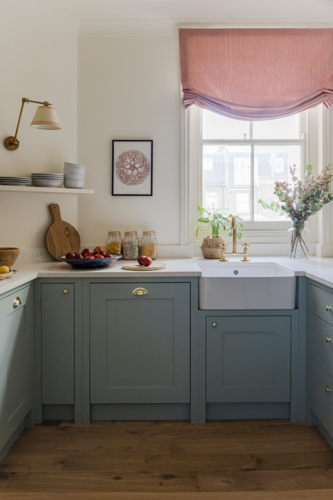 Photo of a mid-sized traditional l-shaped separate kitchen in London with a farmhouse sink, flat-panel cabinets, blue cabinets, quartzite benchtops, white splashback, black appliances, light hardwood floors, no island and yellow benchtop.