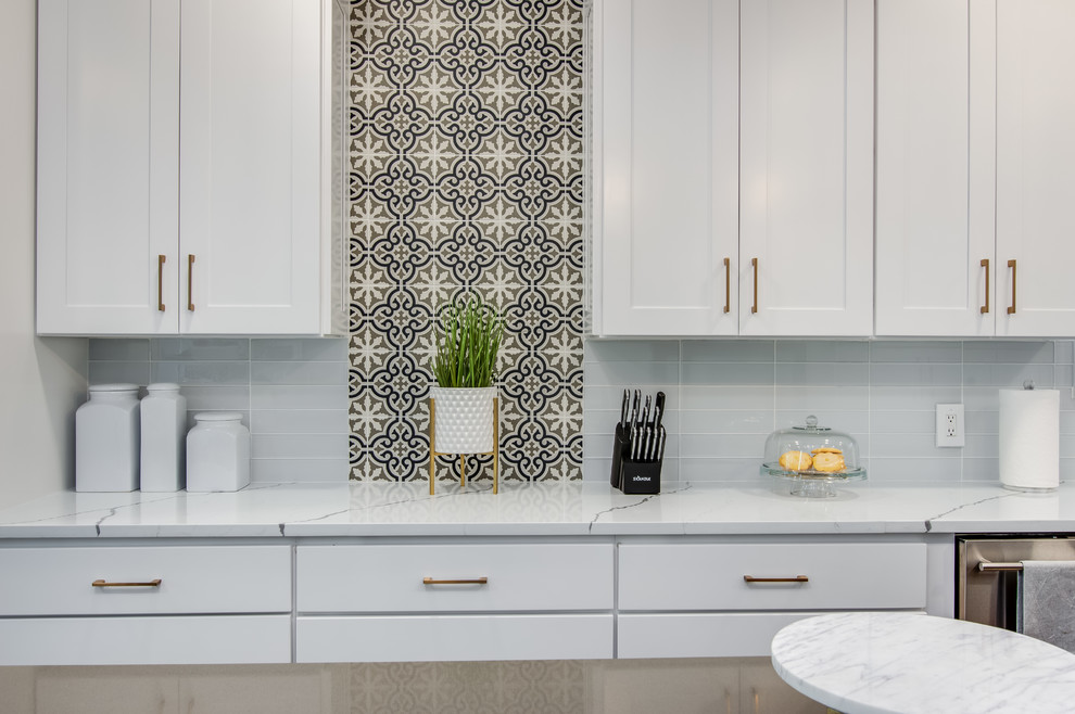 Large transitional l-shaped porcelain tile and gray floor kitchen pantry photo in Houston with a farmhouse sink, shaker cabinets, white cabinets, quartzite countertops, white backsplash, glass tile backsplash, stainless steel appliances, an island and white countertops