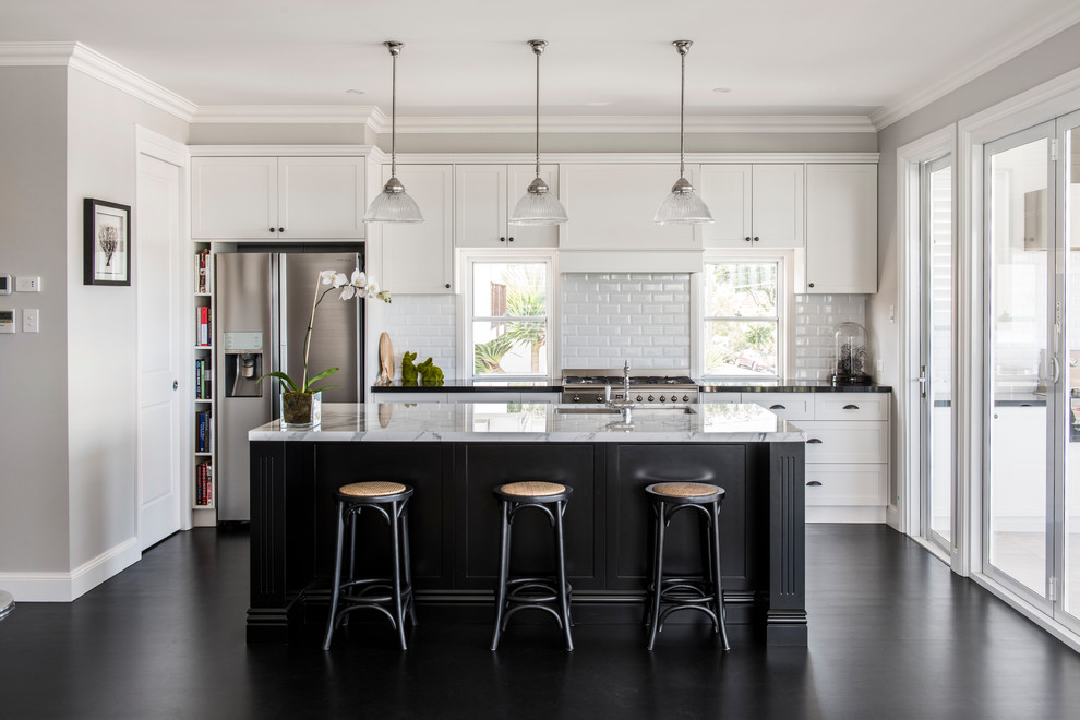 Inspiration for a transitional galley open plan kitchen in Brisbane with an undermount sink, shaker cabinets, white cabinets, white splashback, subway tile splashback, stainless steel appliances, with island and black floor.