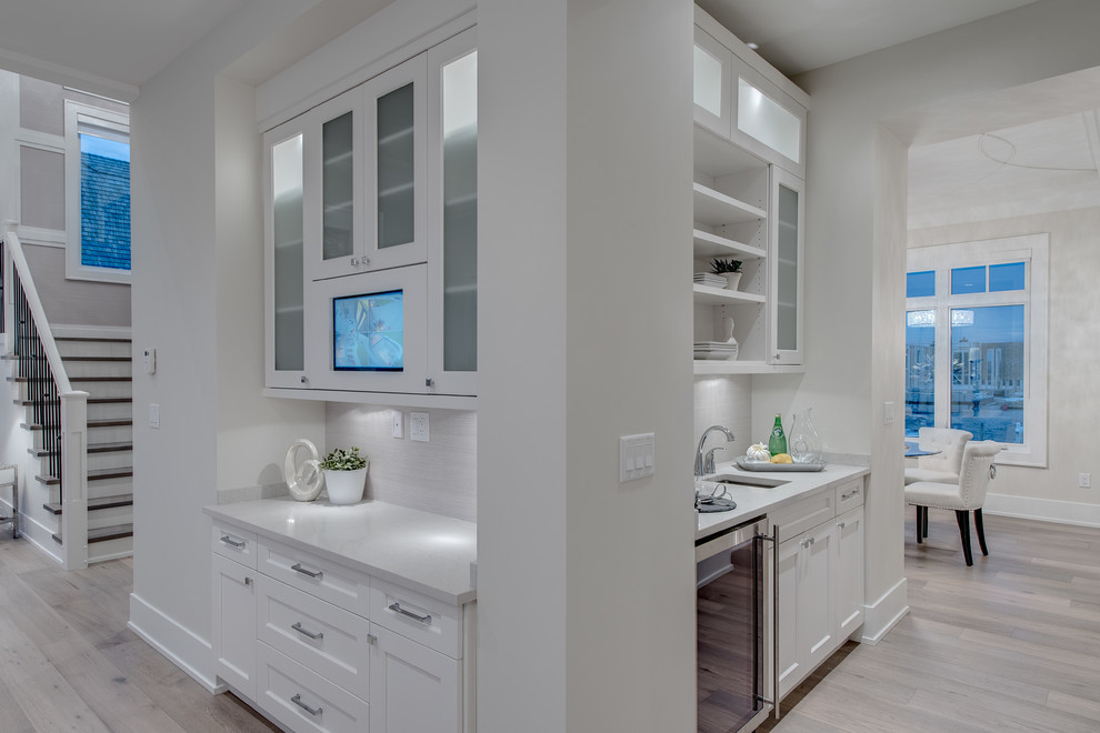 Open concept kitchen - mid-sized transitional u-shaped light wood floor open concept kitchen idea in Vancouver with white cabinets, a single-bowl sink, recessed-panel cabinets, white backsplash, stainless steel appliances and an island