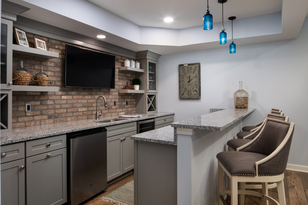 Photo of a mid-sized transitional galley seated home bar in DC Metro with an undermount sink, shaker cabinets, grey cabinets, granite benchtops, brown splashback, brick splashback, medium hardwood floors, brown floor and grey benchtop.