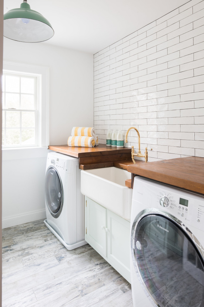 Große Landhausstil Waschküche mit Landhausspüle, Küchenrückwand in Weiß, Rückwand aus Metrofliesen, weißer Wandfarbe, Waschmaschine und Trockner nebeneinander und grauem Boden in Sonstige
