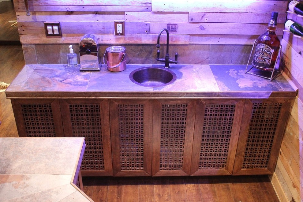 Photo of a large eclectic u-shaped wet bar in Toronto with a drop-in sink, brown cabinets, tile benchtops, brown splashback, ceramic splashback and porcelain floors.