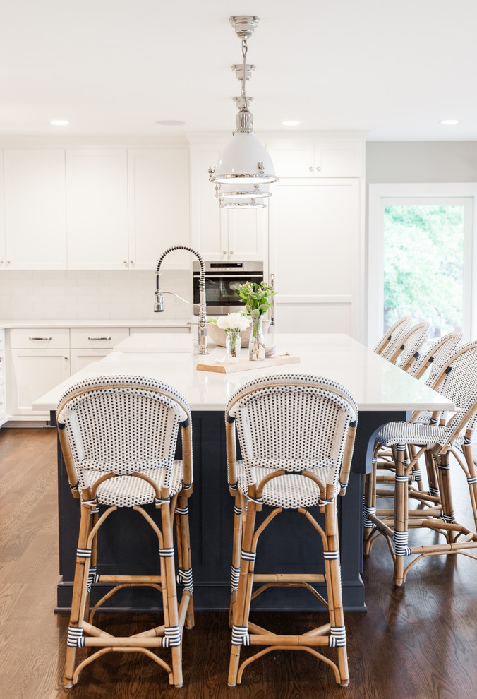 Design ideas for a large beach style l-shaped eat-in kitchen in Minneapolis with a farmhouse sink, shaker cabinets, white cabinets, quartz benchtops, white splashback, subway tile splashback, stainless steel appliances, dark hardwood floors and with island.
