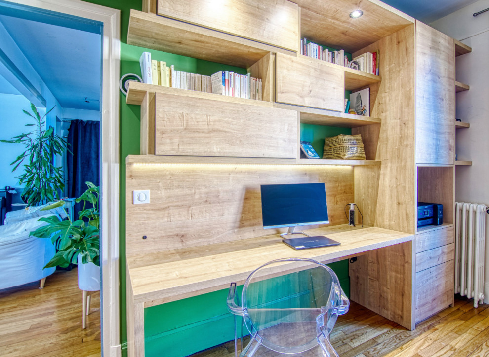 Modern inredning av ett mellanstort hemmabibliotek, med gröna väggar, ljust trägolv, ett inbyggt skrivbord och brunt golv