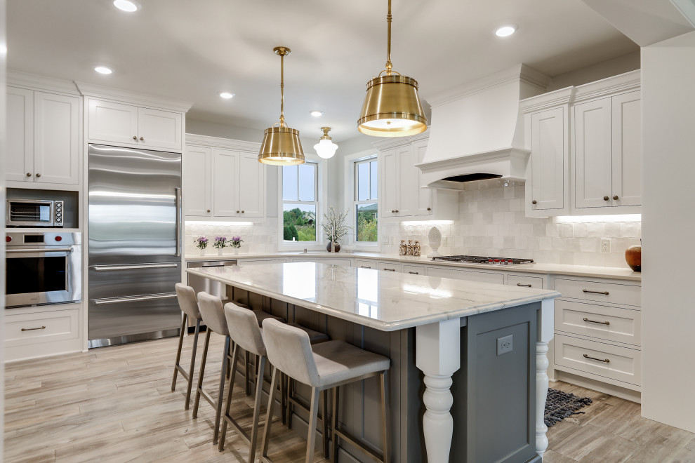 Inspiration for a large transitional l-shaped kitchen in Minneapolis with shaker cabinets, white cabinets, white splashback, stainless steel appliances, light hardwood floors, with island, beige floor and white benchtop.