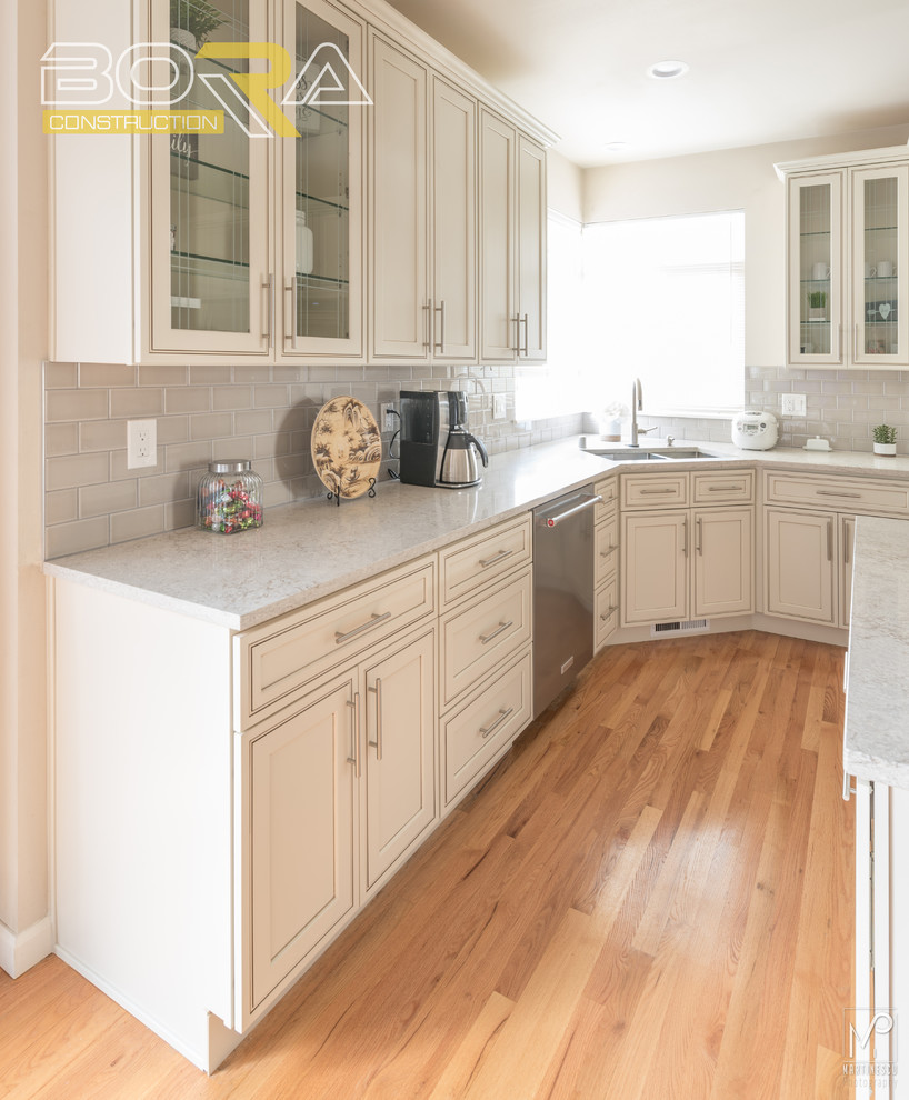 Example of a mid-sized transitional l-shaped eat-in kitchen design with an undermount sink, recessed-panel cabinets, beige cabinets, quartz countertops, gray backsplash, ceramic backsplash, stainless steel appliances and an island