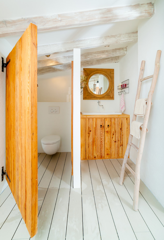 This is an example of a mid-sized mediterranean bathroom in Other with a drop-in sink, flat-panel cabinets, medium wood cabinets, wood benchtops, a two-piece toilet, white walls and painted wood floors.