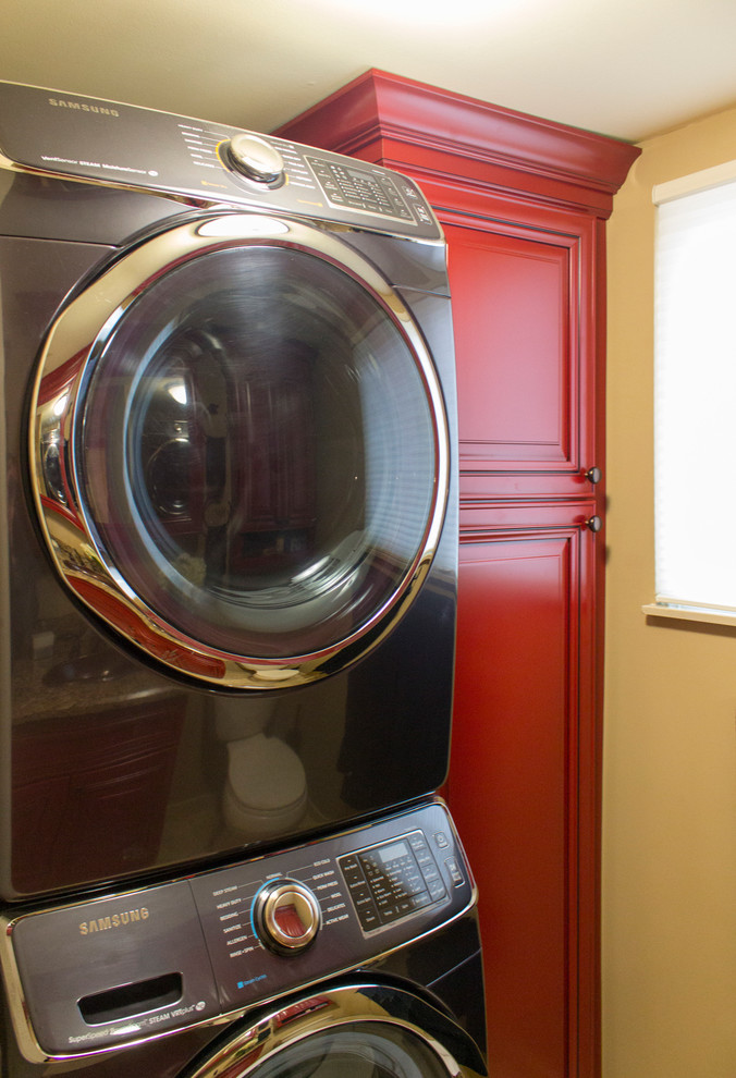 This is an example of a contemporary utility room in Other with a single-bowl sink, raised-panel cabinets, red cabinets, granite benchtops, beige walls, limestone floors and a stacked washer and dryer.