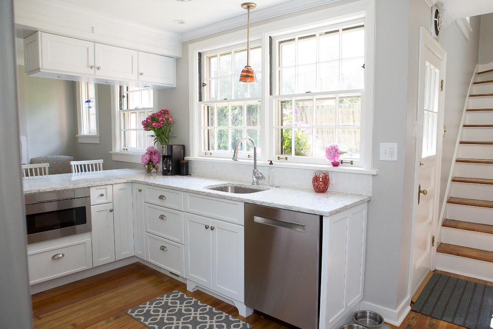 Example of a small transitional light wood floor kitchen design with an undermount sink, shaker cabinets, white cabinets, quartz countertops, white backsplash, ceramic backsplash, stainless steel appliances and a peninsula