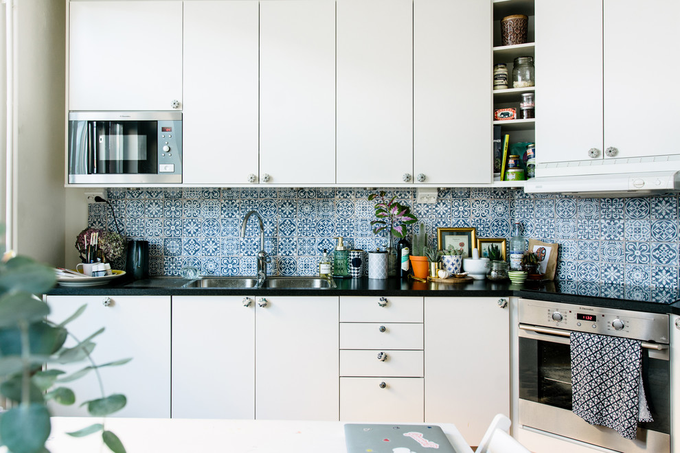 Design ideas for a mid-sized mediterranean single-wall eat-in kitchen in Stockholm with a double-bowl sink, flat-panel cabinets, white cabinets, granite benchtops, multi-coloured splashback, porcelain splashback, stainless steel appliances and no island.