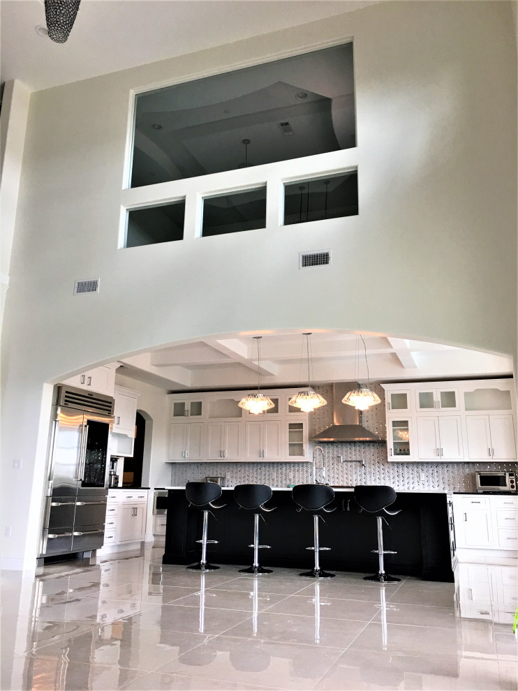 Kitchen - large eclectic l-shaped porcelain tile, beige floor and coffered ceiling kitchen idea in Austin with a farmhouse sink, shaker cabinets, white cabinets, quartz countertops, white backsplash, mosaic tile backsplash, stainless steel appliances, an island and black countertops