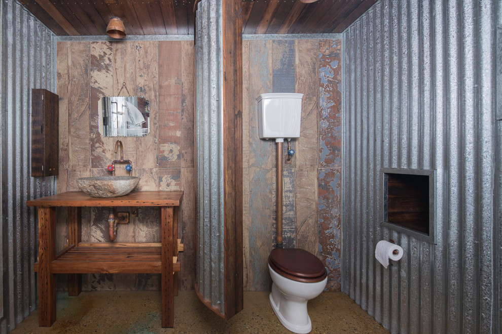Photo of an industrial bathroom in Canberra - Queanbeyan with open cabinets, medium wood cabinets, a two-piece toilet, brown walls, concrete floors, a vessel sink, wood benchtops, brown benchtops and brown floor.