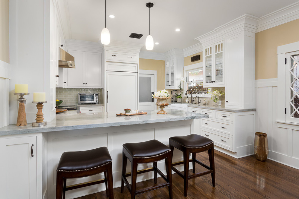 Inspiration for a timeless u-shaped brown floor and medium tone wood floor kitchen remodel in Los Angeles with a farmhouse sink, shaker cabinets, white cabinets, gray backsplash, a peninsula, marble countertops, ceramic backsplash and white appliances