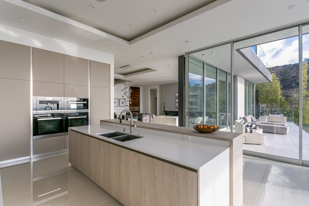 Design ideas for a mid-sized modern l-shaped open plan kitchen in Los Angeles with a double-bowl sink, flat-panel cabinets, beige cabinets, quartz benchtops, white splashback, stainless steel appliances, ceramic floors and with island.