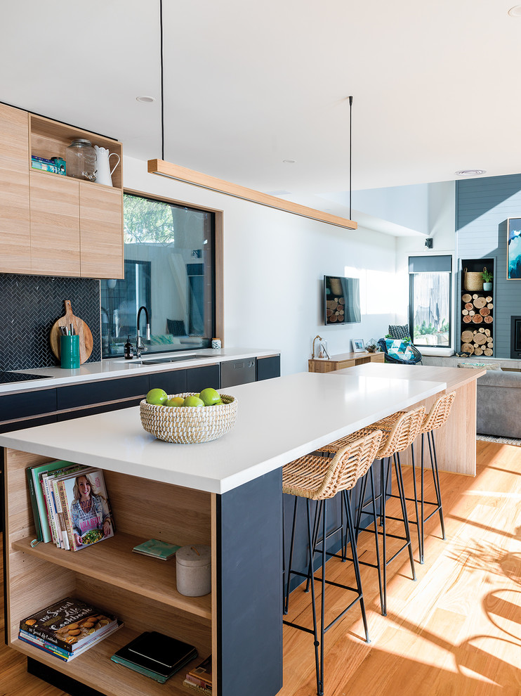 Inspiration for a large beach style galley open plan kitchen in Other with an undermount sink, black cabinets, black splashback, mosaic tile splashback, stainless steel appliances, with island, white benchtop, flat-panel cabinets, medium hardwood floors, brown floor and quartz benchtops.