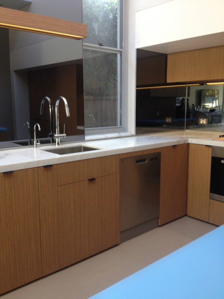 Mid-sized contemporary l-shaped eat-in kitchen in Sydney with an undermount sink, flat-panel cabinets, medium wood cabinets, solid surface benchtops, grey splashback, mirror splashback, stainless steel appliances, medium hardwood floors and with island.