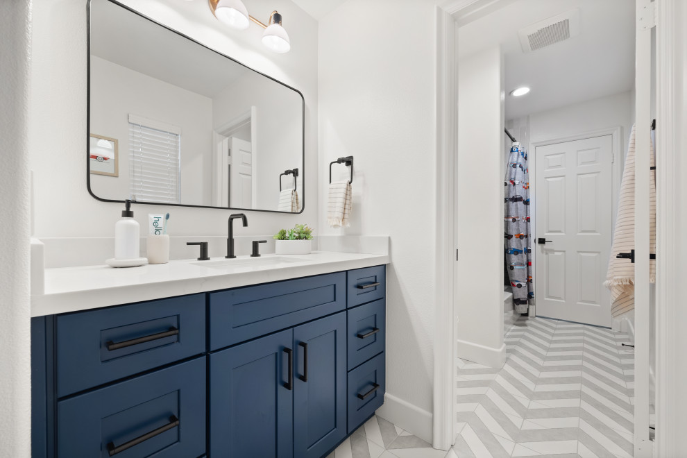 Cette photo montre une salle de bain moderne de taille moyenne pour enfant avec un placard à porte shaker, des portes de placard bleues, une baignoire posée, un combiné douche/baignoire, un carrelage bleu, des carreaux de céramique, un mur blanc, un sol en carrelage de porcelaine, un lavabo posé, un sol gris, une cabine de douche avec un rideau, un plan de toilette blanc, des toilettes cachées, meuble simple vasque et meuble-lavabo encastré.