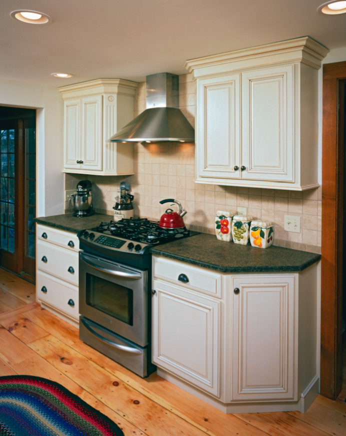 Mid-sized transitional galley light wood floor eat-in kitchen photo with a farmhouse sink, raised-panel cabinets, white cabinets, soapstone countertops, beige backsplash, stone tile backsplash and stainless steel appliances