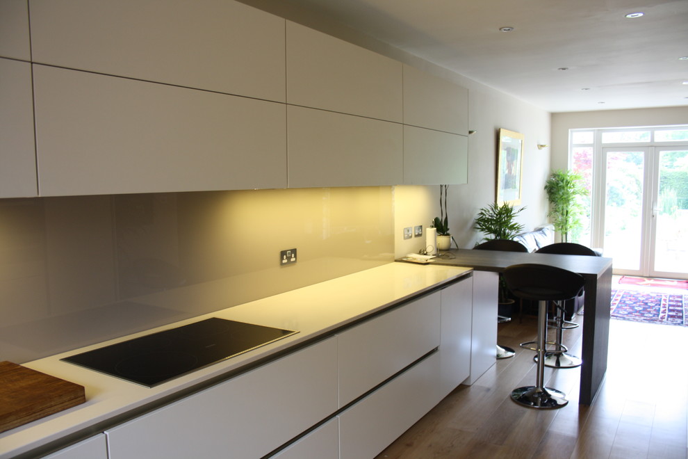 Design ideas for a mid-sized contemporary u-shaped open plan kitchen in London with an undermount sink, flat-panel cabinets, black cabinets, solid surface benchtops, beige splashback, glass sheet splashback, stainless steel appliances, light hardwood floors and a peninsula.