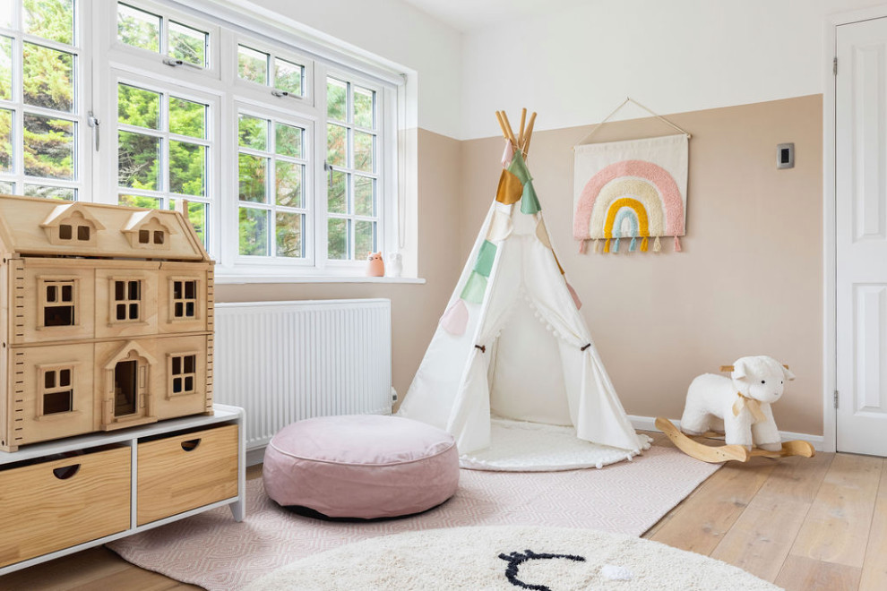Medium sized rural children’s room for girls in Surrey with pink walls, light hardwood flooring and beige floors.